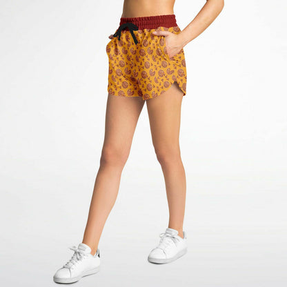 Women’s shorts featuring a pizza design of pizza pies and pizza slices on a yellow background with a red waistband and red outer pocket with a slice of pizza.