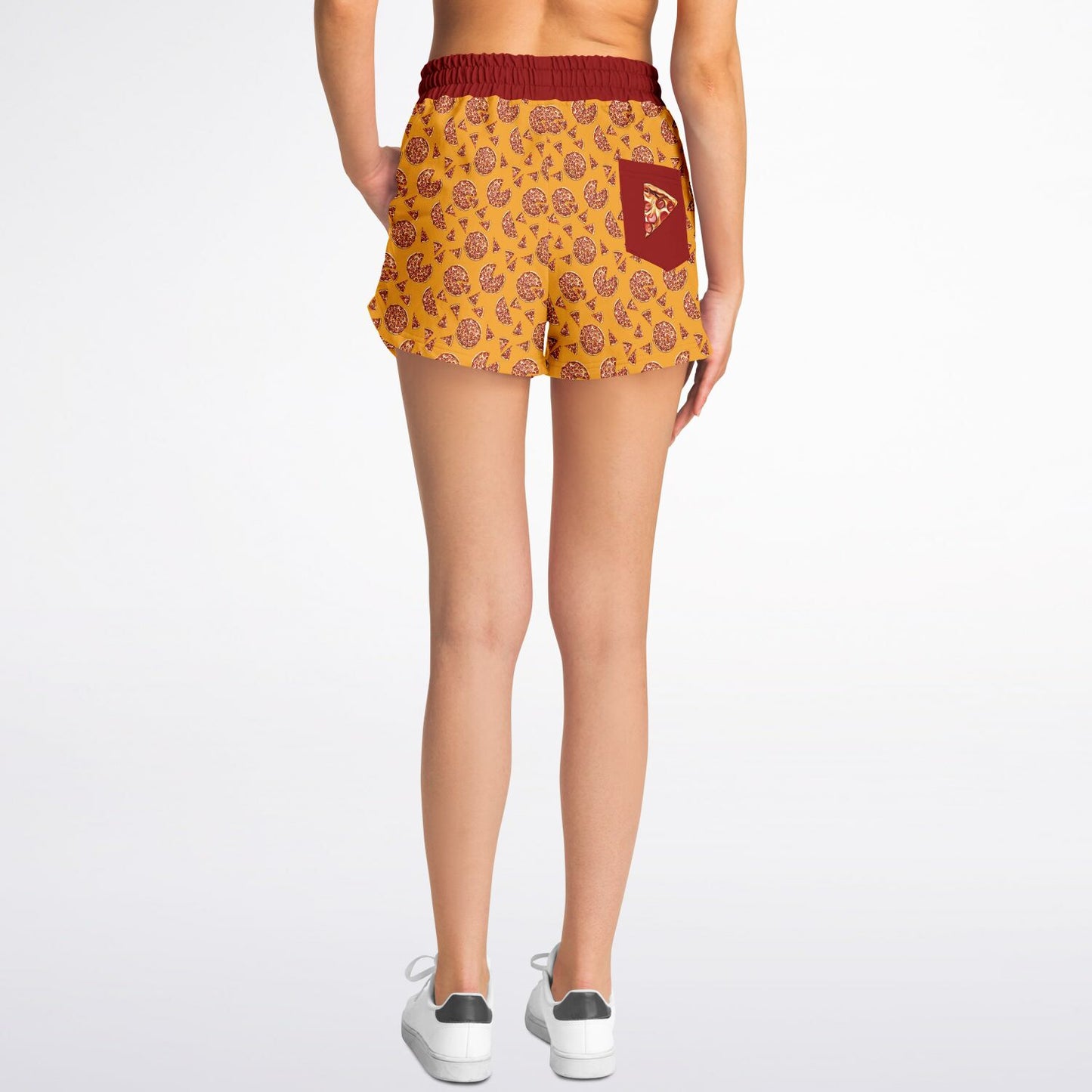 Women’s shorts featuring a pizza design of pizza pies and pizza slices on a yellow background with a red waistband and red outer pocket with a slice of pizza.