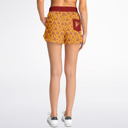 Women’s shorts featuring a pizza design of pizza pies and pizza slices on a yellow background with a red waistband and red outer pocket with a slice of pizza.