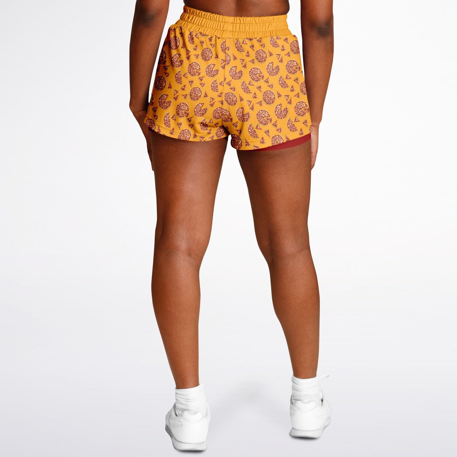 Women's shorts featuring a pizza design of pizza pies and pizza slices on a yellow background with a red undershort.