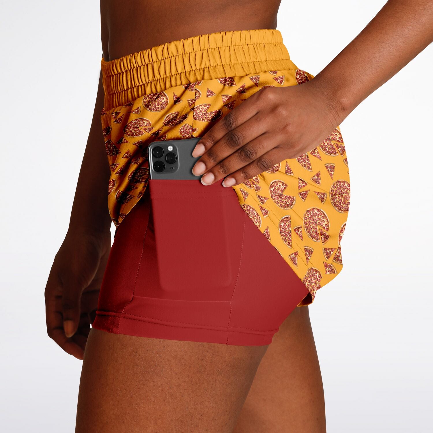 Women's shorts featuring a pizza design of pizza pies and pizza slices on a yellow background with a red under short that features a phone pocket.