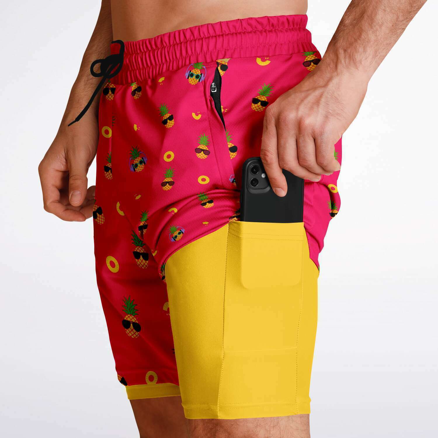 Men's 2-in-1 Shorts. These fun shorts feature a pink background with pineapples wearing a variety of sunglasses. Shorts have a black drawstring and zip up pockets.